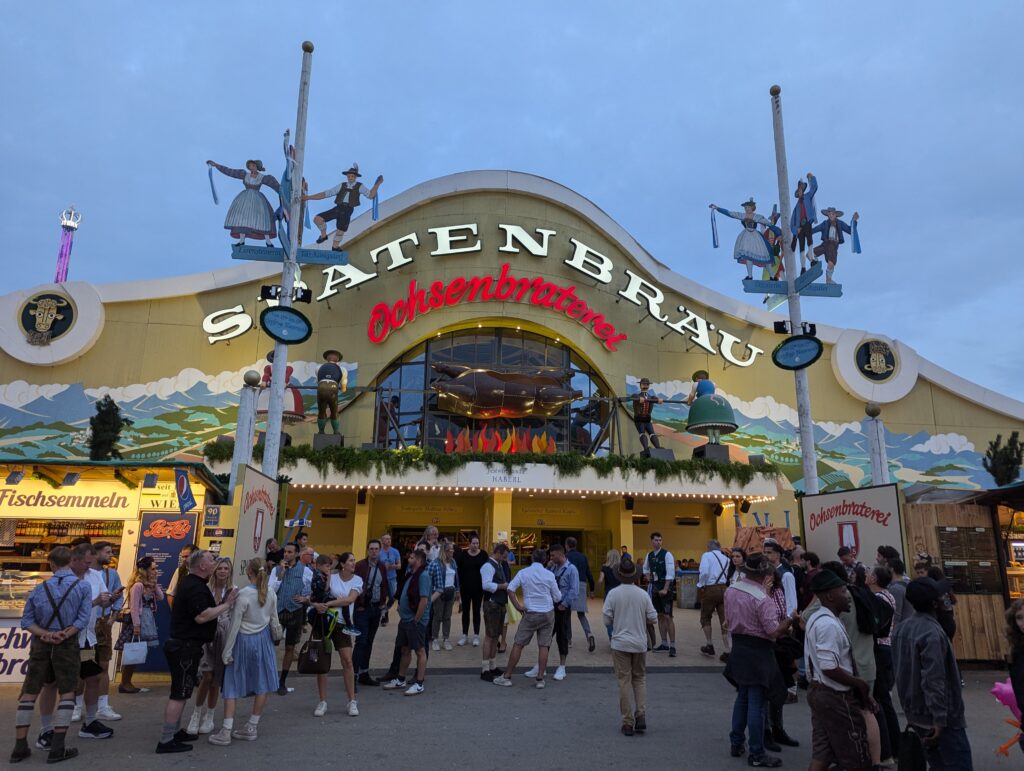Spaten-Bräu Ochsenbraterei tent exterior at Oktoberfest with crowds gathering at dusk