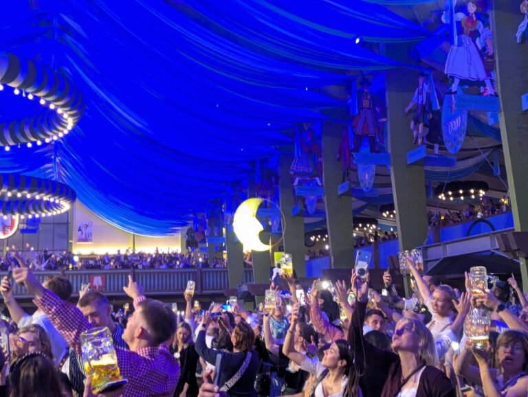Revellers raising Mass beers under the blue draped ceiling of an Oktoberfest tent